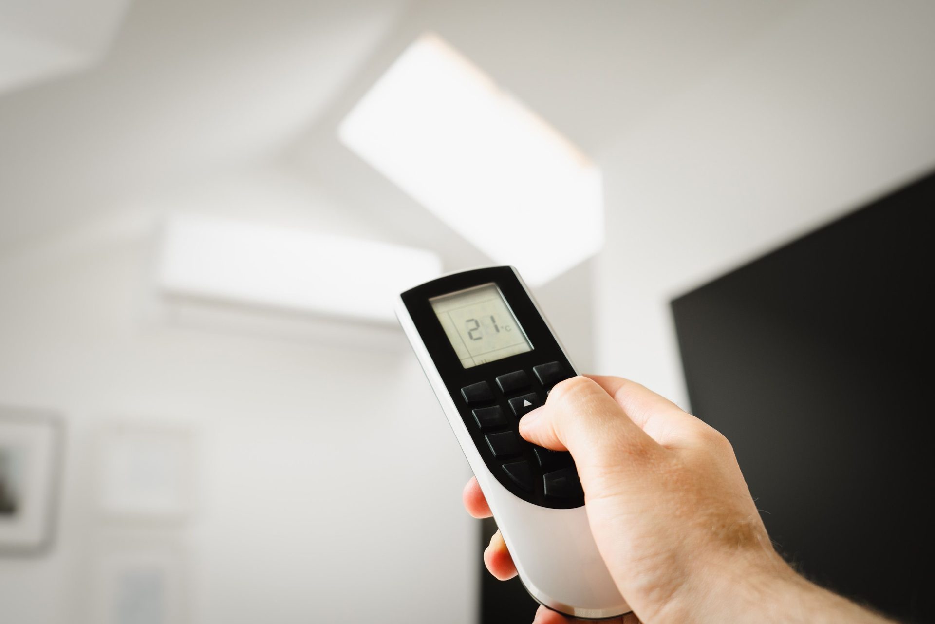 Gros plan sur un homme utilisant une télécommande pour régler la climatisation à l'intérieur.