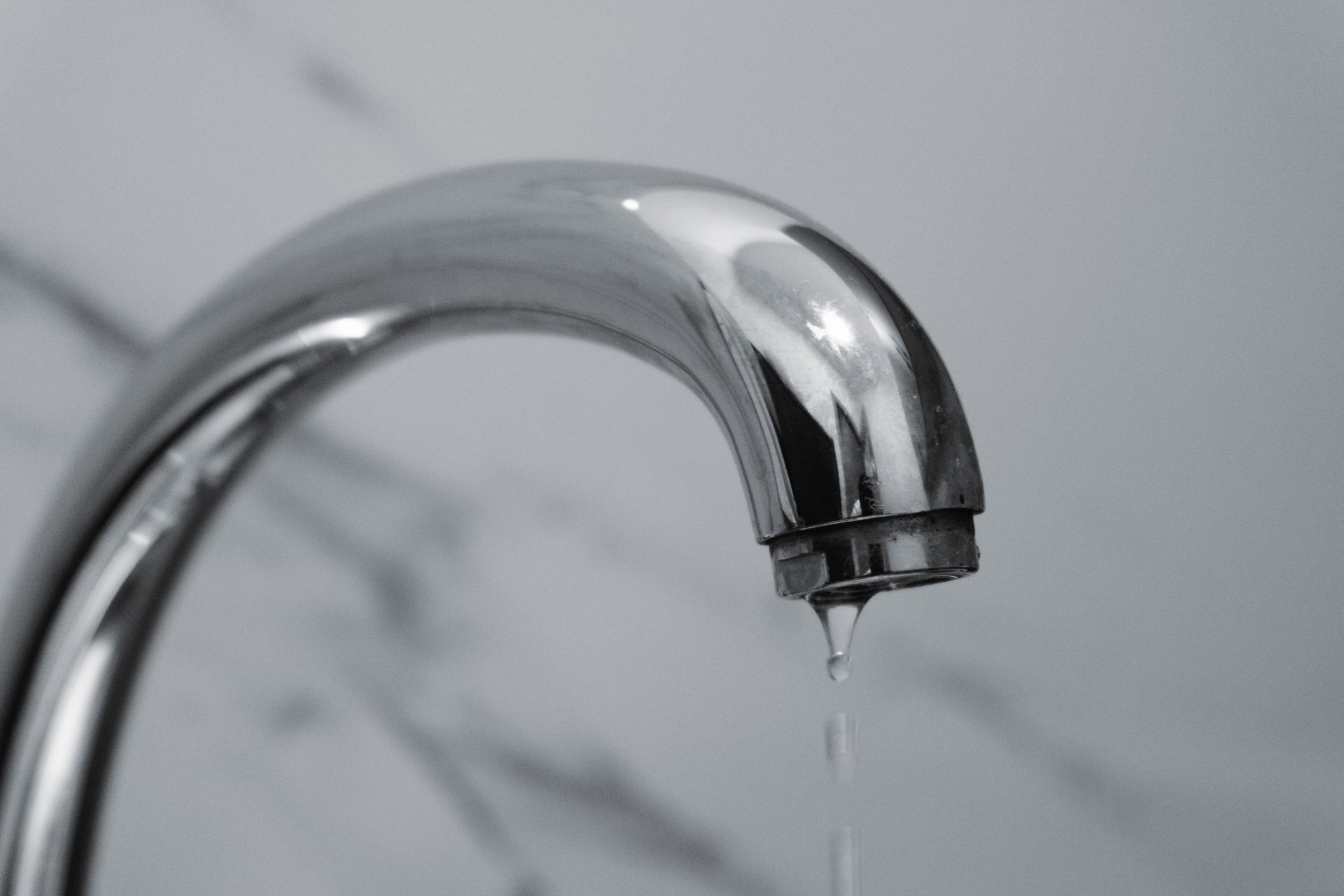 Gros plan sur un robinet de salle de bains moderne en chrome, avec de l'eau qui goutte de l'extrémité.