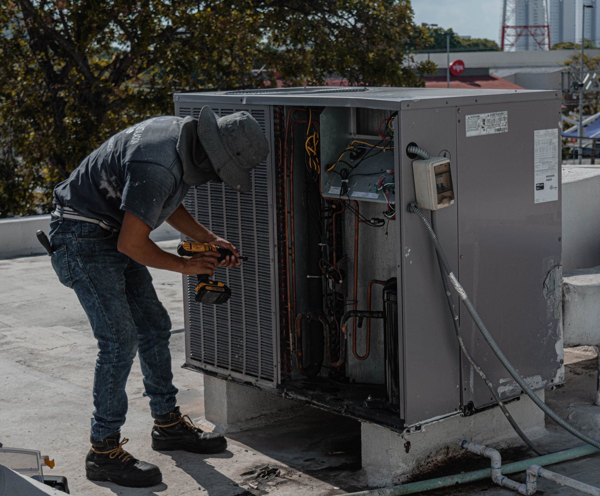 Un ouvrier portant un bob répare une unité de climatisation extérieure sur un toit.