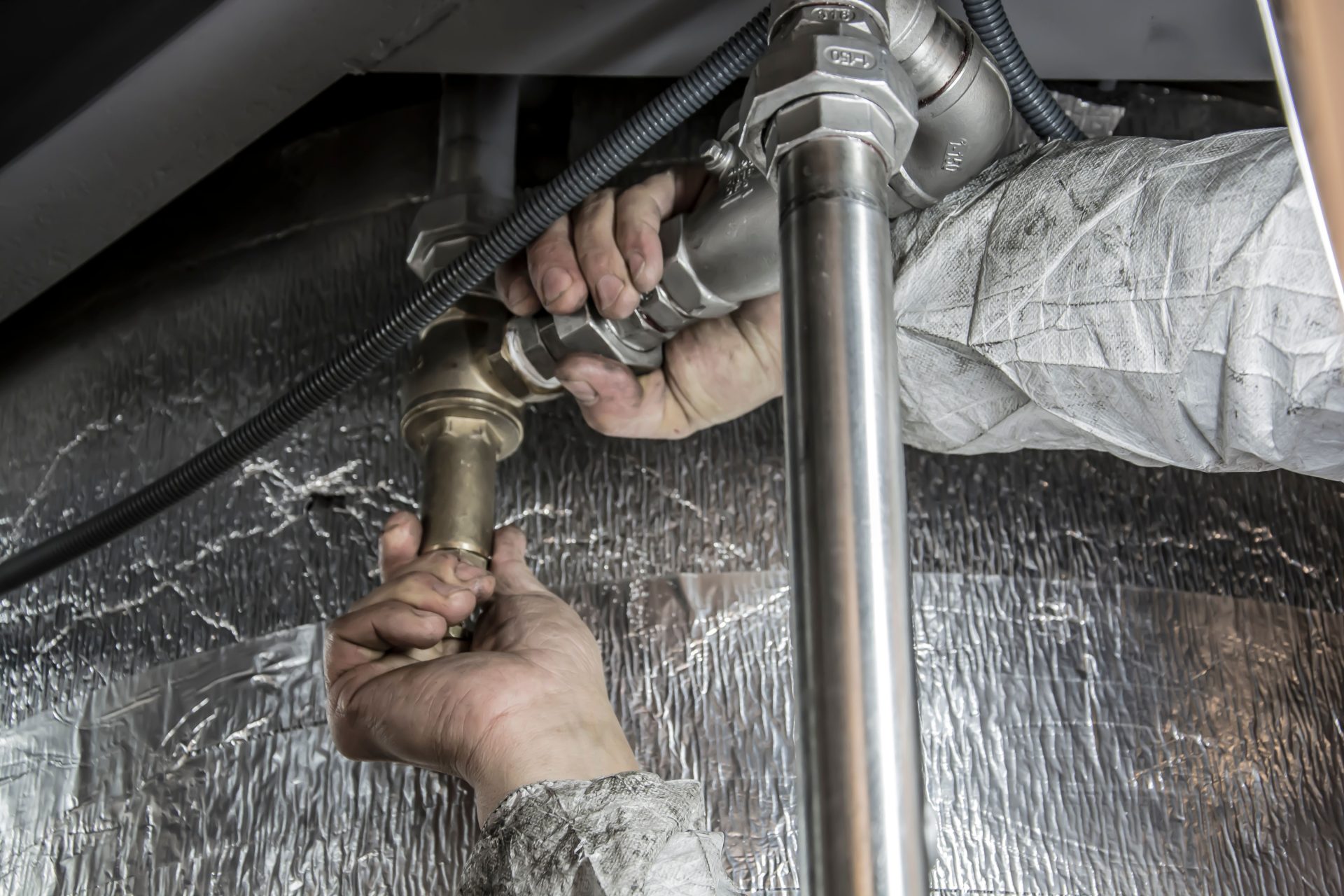 Gros plan sur les mains d'un plombier installant des tuyaux en acier à l'intérieur, illustrant un travail manuel qualifié.