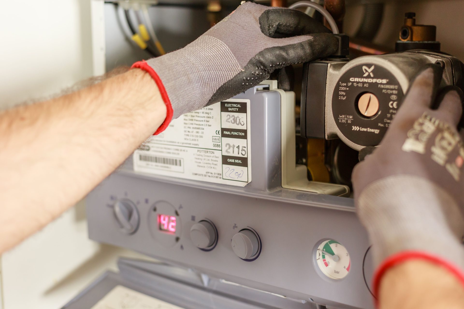 Gros plan sur des mains réglant une chaudière à l'aide d'instruments de précision, illustrant des travaux de maintenance.